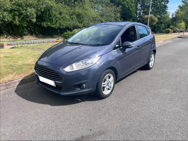 Blue Ford Fiesta parked on a residential road with greenery in the background.