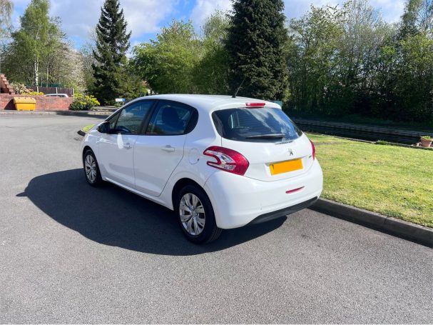 A white hatchback parked on a residential street with greenery in the background.