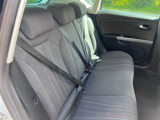 Empty back seat of a car with three seat belts.