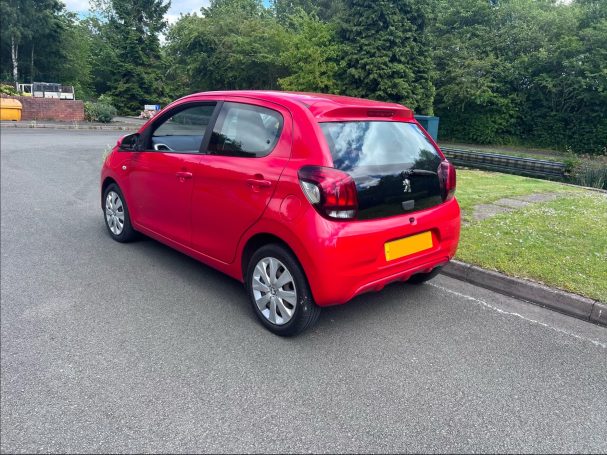 Red compact car parked on a quiet street with greenery in the background.