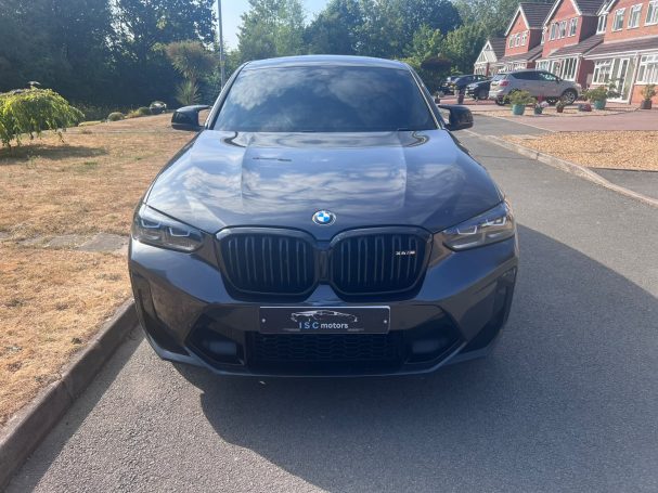 Grey BMW parked on a quiet road with greenery in the background.