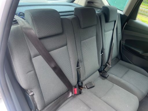 Grey upholstered back seats of a car with seatbelts.