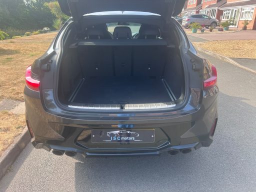 Grey BMW parked on a quiet road with greenery in the background.