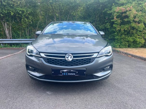 A grey Astra parked in front of green bushes