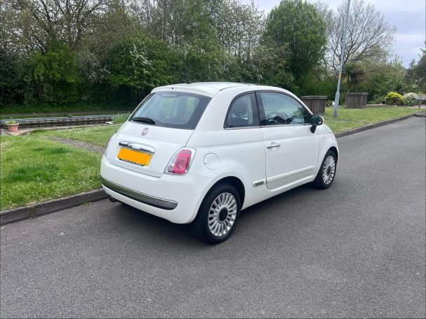 White compact car parked on a roadside with greenery in the background.