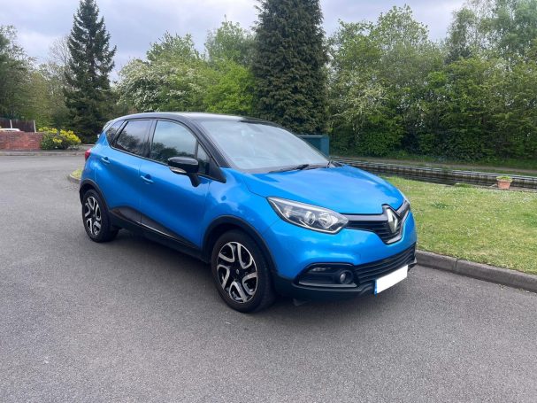 A blue Renault SUV parked on a road surrounded by greenery.