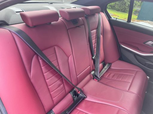 Red leather backseat of a car with seatbelts.