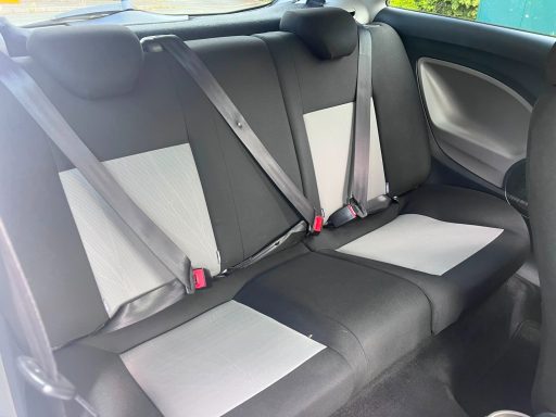 Interior view of a car's back seat with three seat belts and grey seat covers.