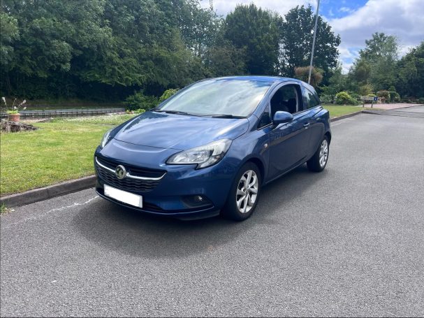 Blue car parked on a grassy area with trees in the background.