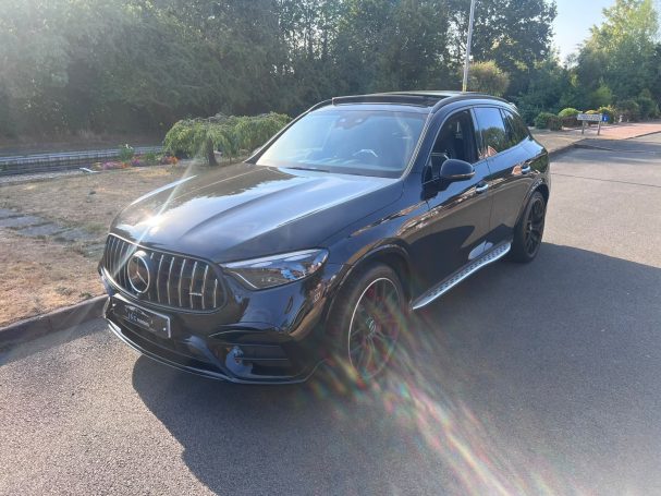 Black Mercedes parked on a quiet road with greenery in the background
